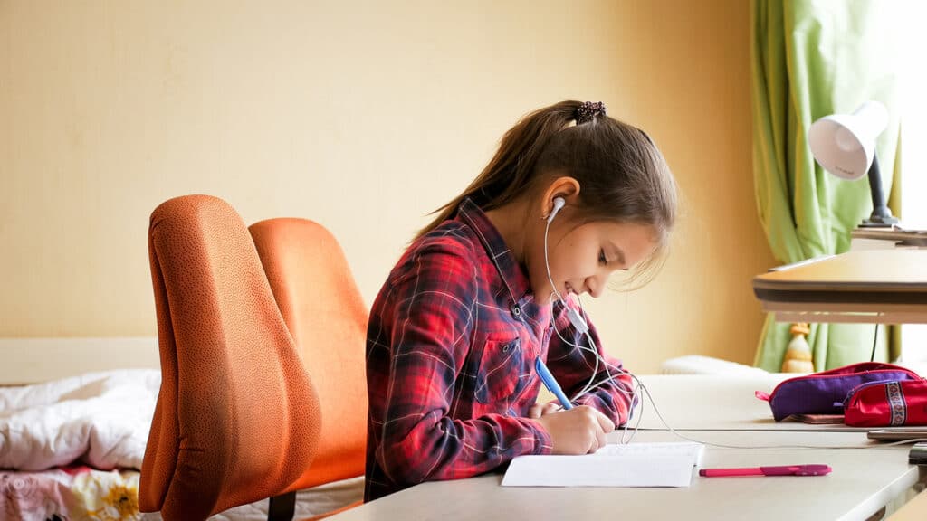 young girl writing in a book with headphones in