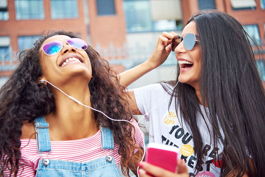 two girls sharing headphones laughing