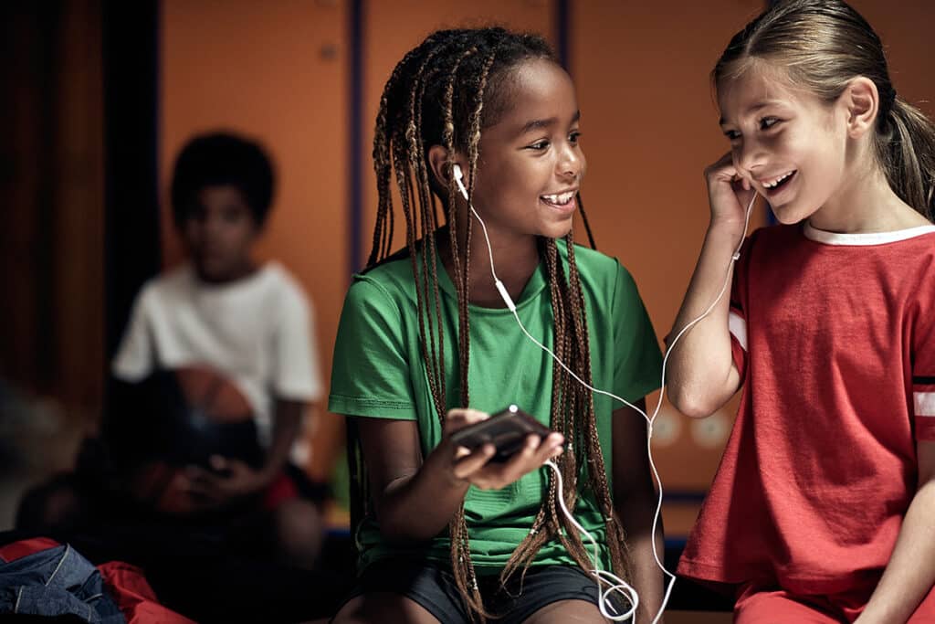 two smiling girls sharing headphones