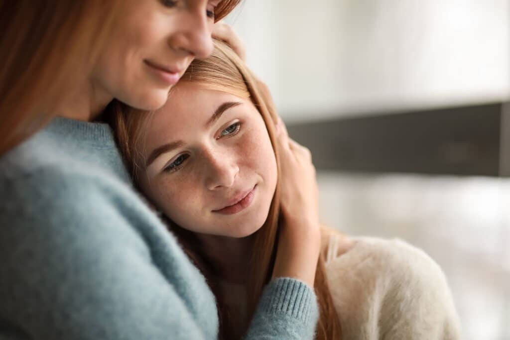 young teen girl being embraced by her mother