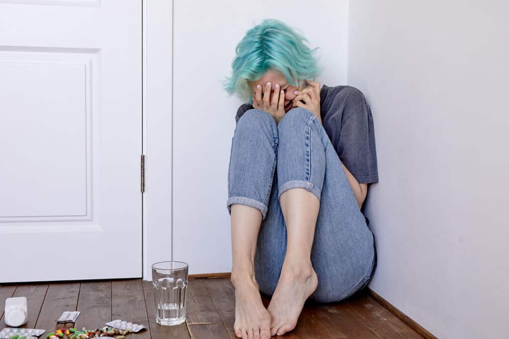 teen girl with blue hair with drugs and pills crying in a corner