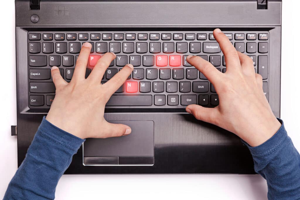 young hands typing on a keyboard with the letters for porn in red
