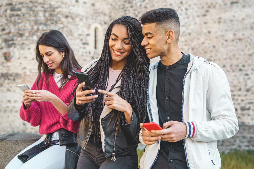 three teens smiling at their phones