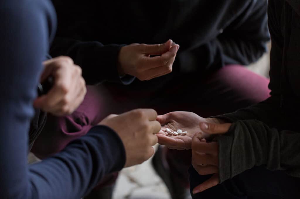 three peoples hands holding pills in a circle