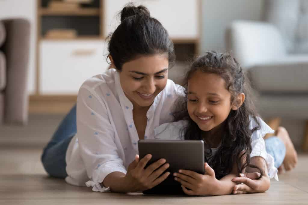 mother and daughter smiling as they look at a tablet