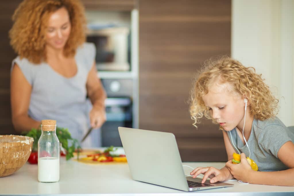 daughter is on laptop while mom makes food at counter