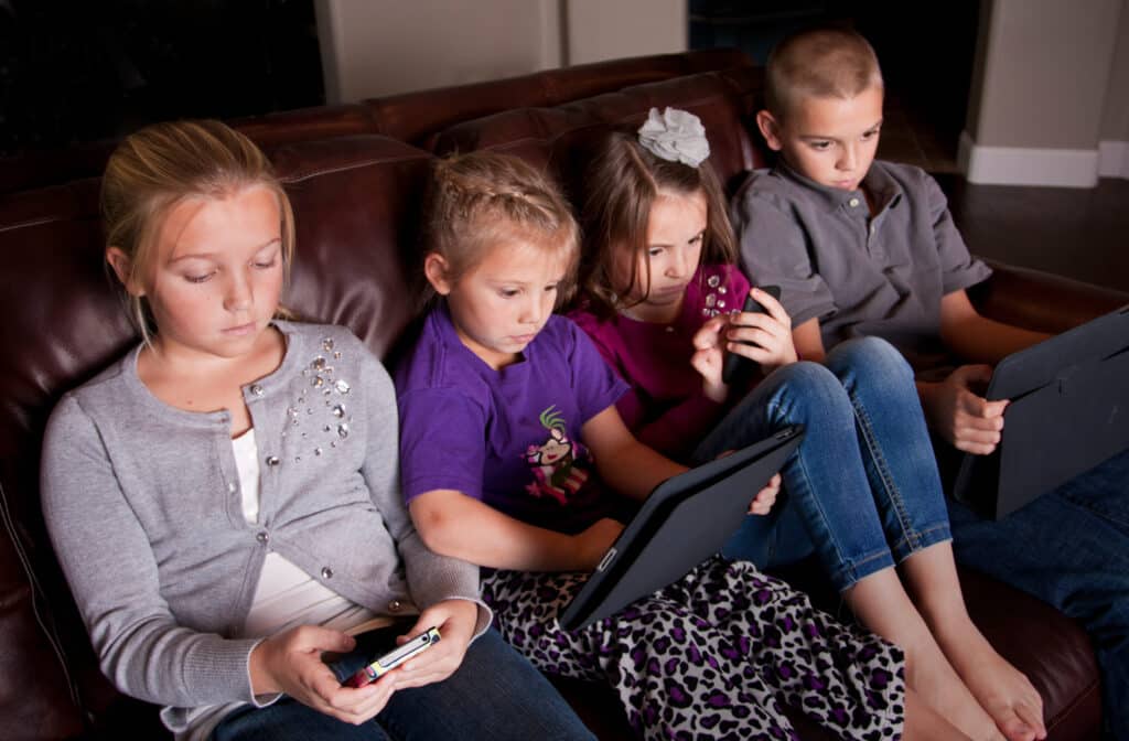 four kids on couch engrossed in technology