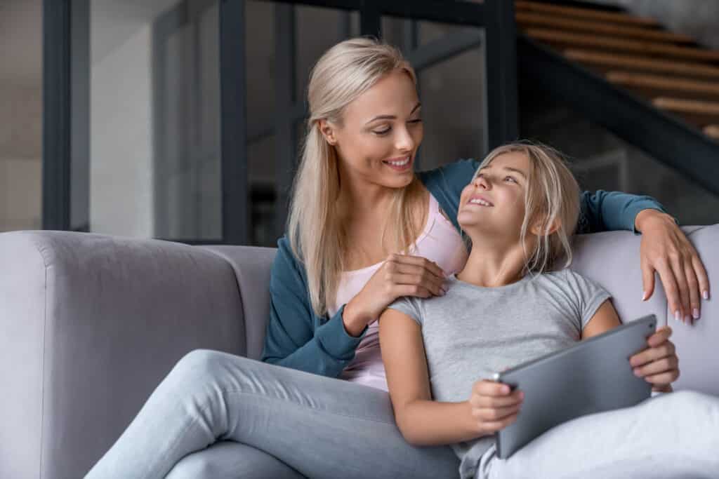 mom and daughter sitting on couch with tablet smiling at each other
